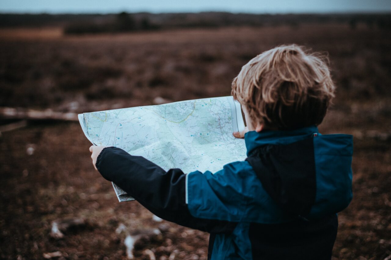 A small child (wearing a blue and black coat) looking at a map.