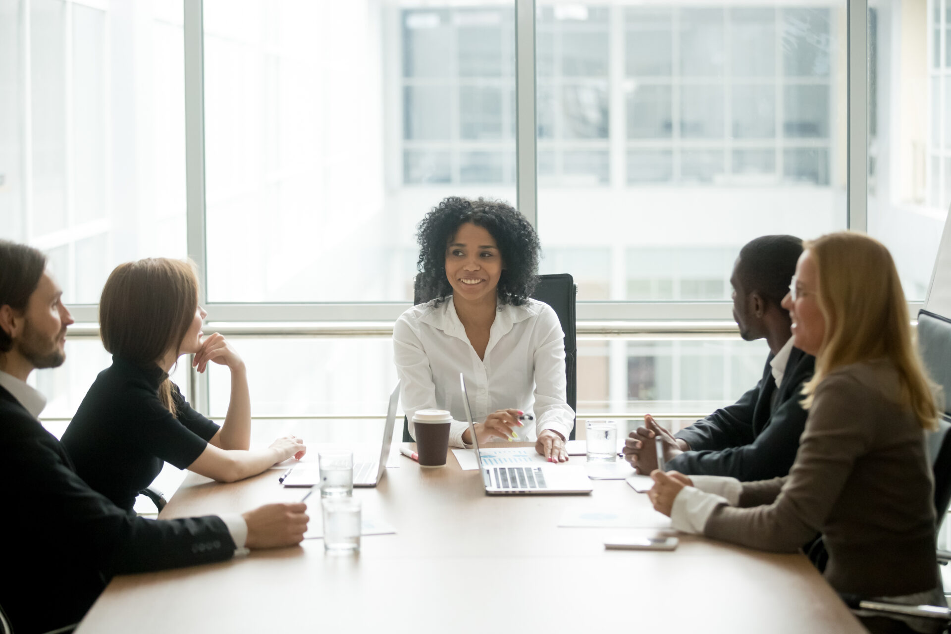 Five people sitting around a board table with laptops, looking engaged in conversation.