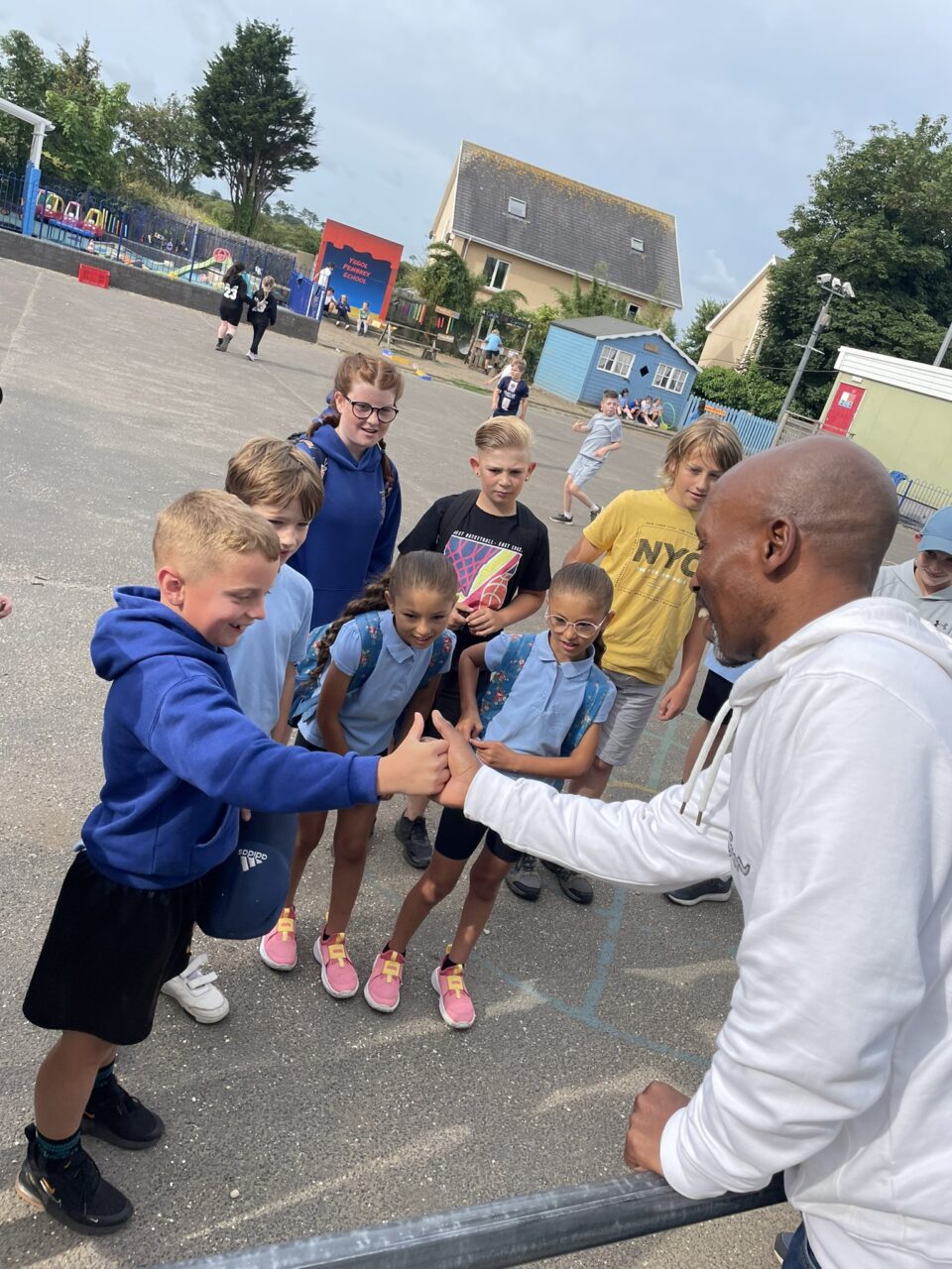 A group of young school children in blue uniforms watching one boy play a hand game with a man.