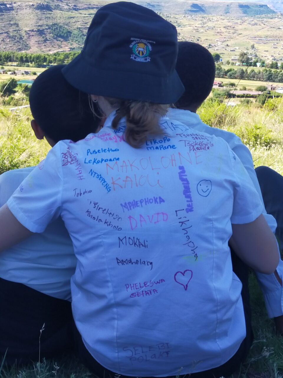A back shot of 3 people. One is wearing a signed shirt and is wearing a bucket hat.