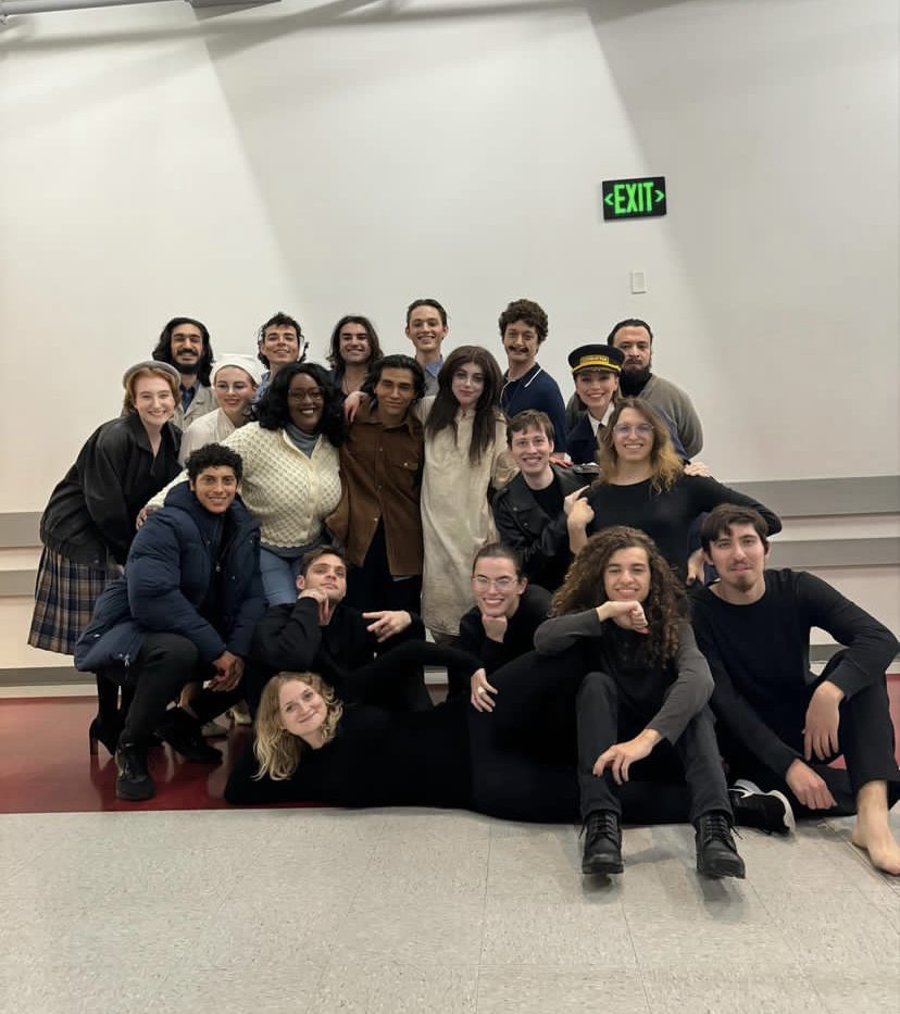 A big group of young people smiling for a photo. One person is lying down in the front of the group.