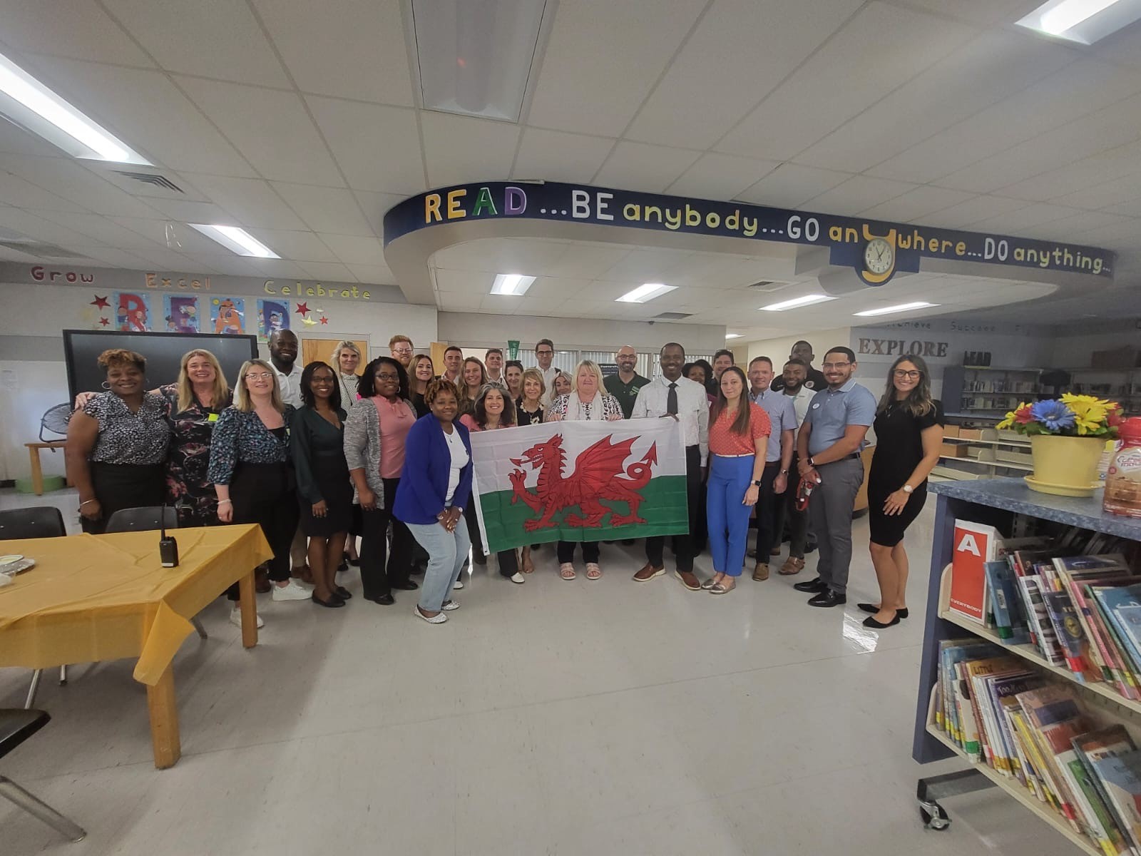 A group of people standing in a classroom holding a Welsh flag