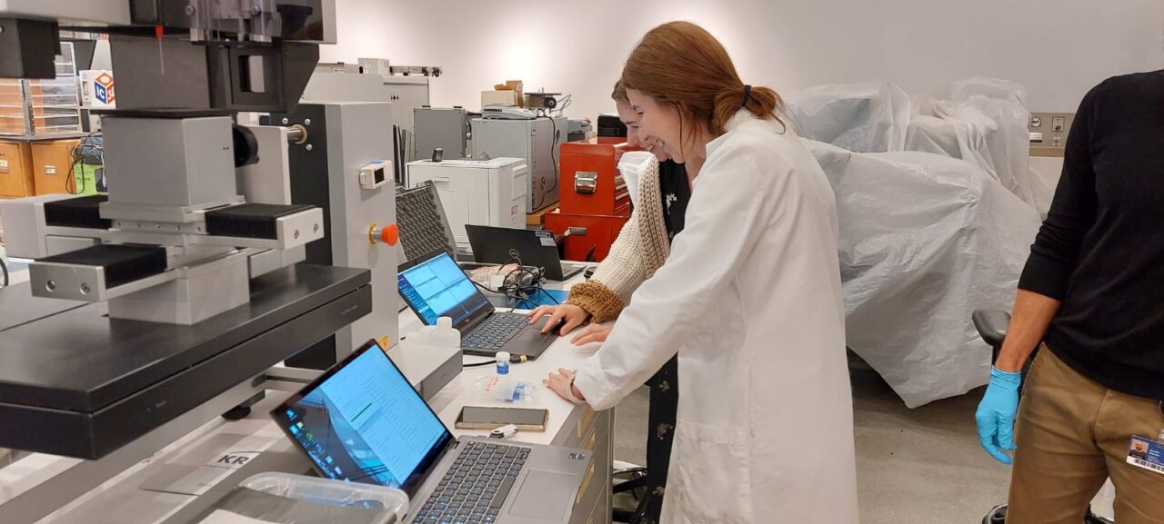 Two women wearing white coats looking at a laptop in a laboratory and smiling.