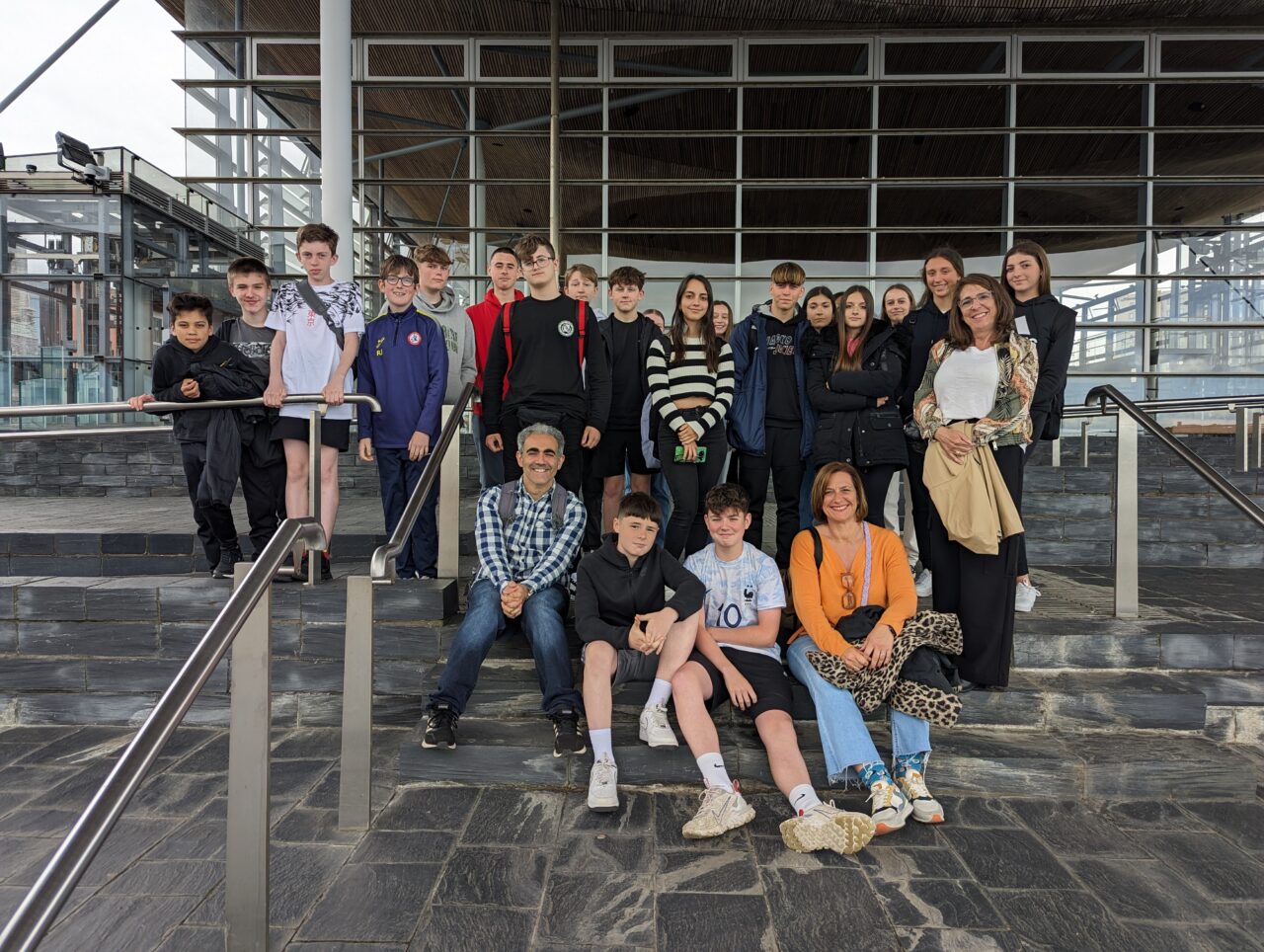 A group of Spanish and Welsh pupils and their teachers sat outside the Senedd building in Cardiff