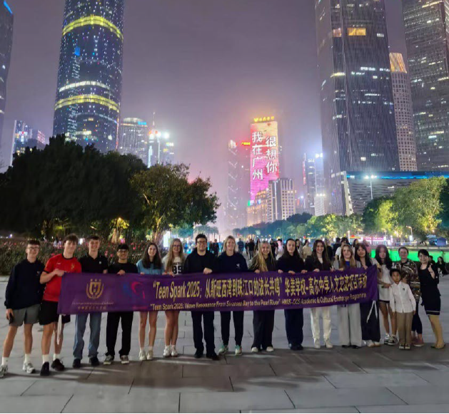 Teen Spark 2025 participants hold a programme banner in a city plaza at night, with illuminated skyscrapers and a skyline backdrop in Guangzhou.