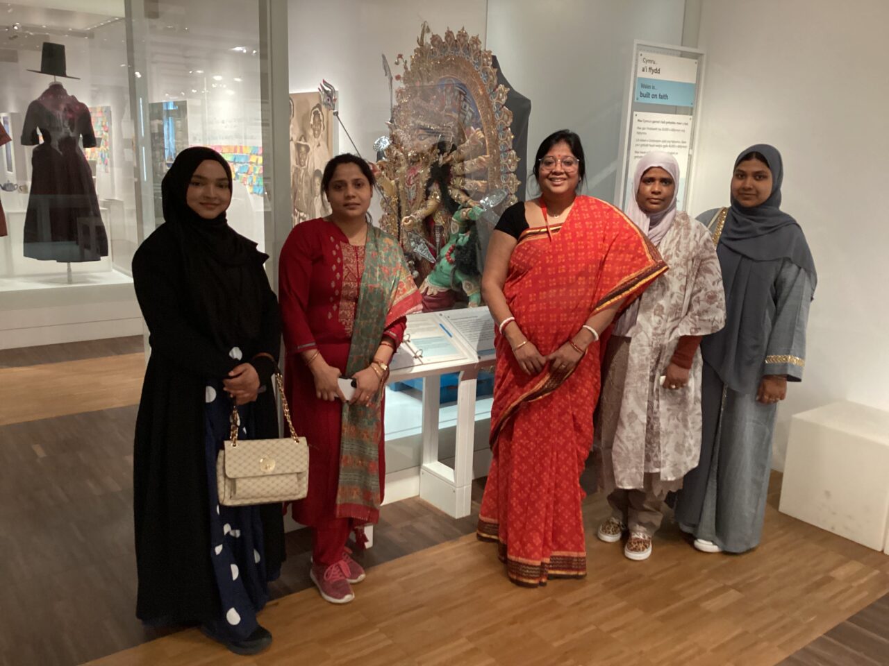 Group photograph taken inside St Fagan’s museum exhibition. Five people stand next to a display featuring an ornate traditional sculpture, with additional artworks and exhibits visible in the gallery behind them.