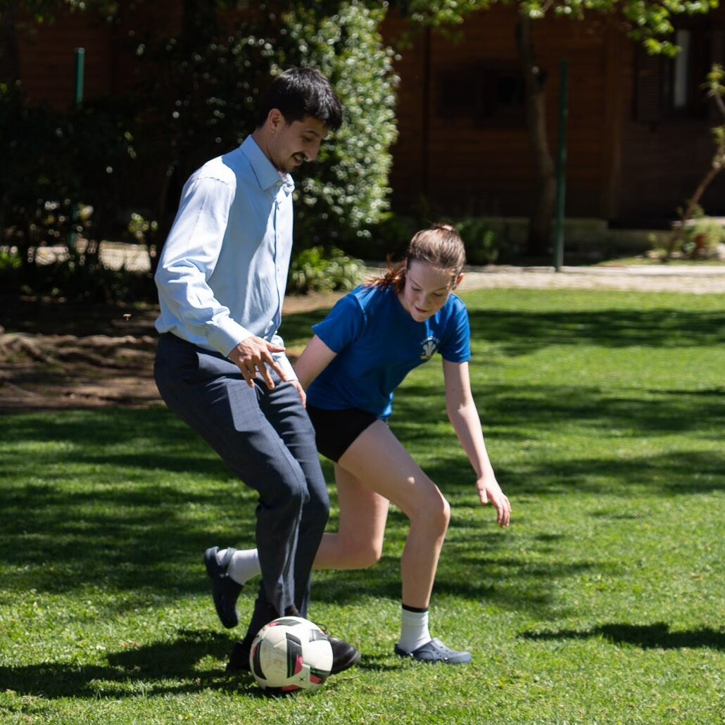 Two participants play football at the British Ambassador's residence in Lisbon, with trees and buildings in the background.