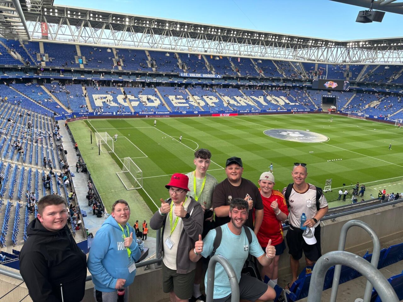 Small group posing in the stands of RCD Espanyol's football stadium, with the pitch and blue seating visible in the background.