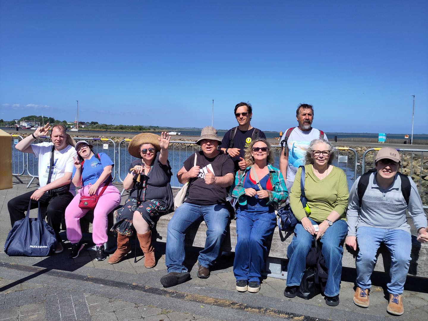 Group of participants from The Tenby Project CIC sitting together on a waterfront promenade in Ireland during their international learning visit.