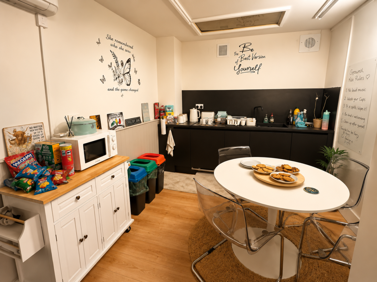 Welcoming kitchen and communal space featuring a dining table, refreshments, snacks, and kitchen facilities. Inspirational messages on the walls and a tray of biscuits create a comfortable environment for visitors to gather and connect.