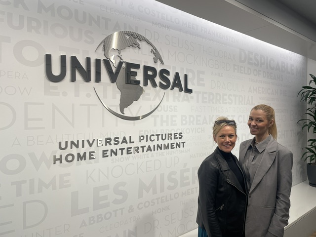 Marlen Komorowski and Sara Pepper standing in front of a wall displaying the Universal Pictures Home Entertainment logo inside an office building.